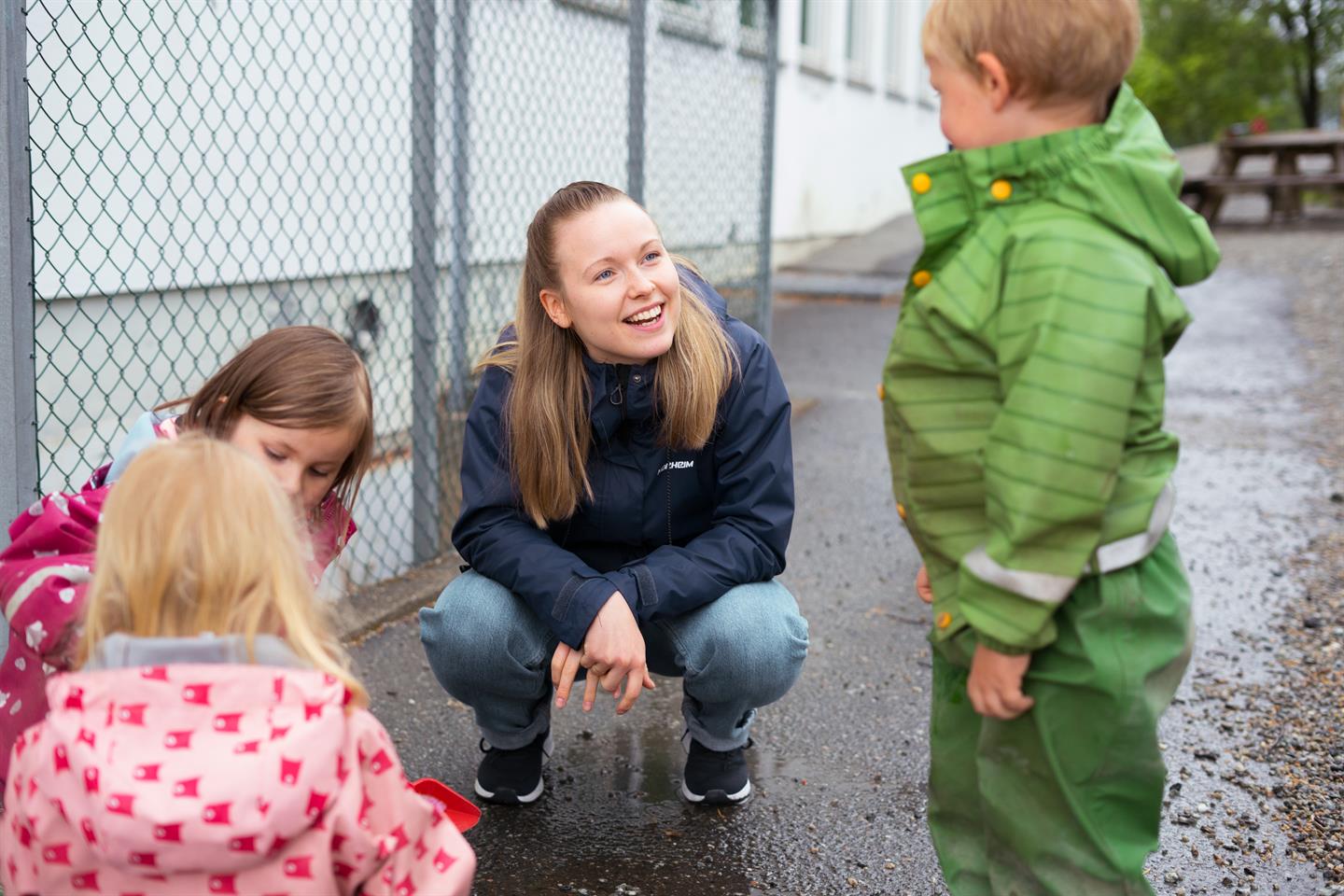 Student sammen med tre barnehagebarn i regnt&oslash;y